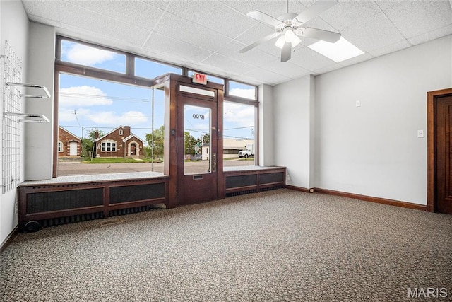 carpeted spare room featuring ceiling fan, a drop ceiling, baseboards, and expansive windows