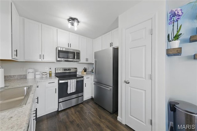 kitchen with appliances with stainless steel finishes, dark wood-style floors, white cabinetry, light countertops, and a sink