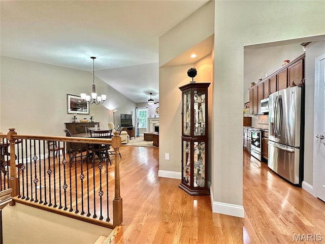 corridor featuring light wood-style floors, vaulted ceiling, a chandelier, and baseboards