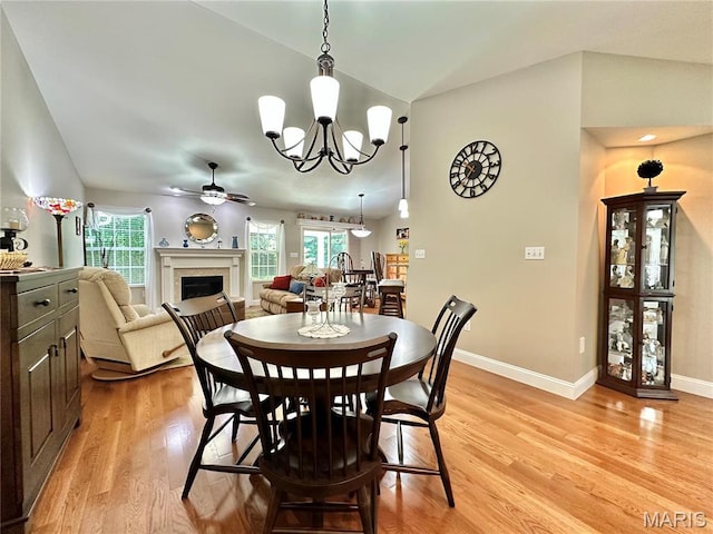 dining space with light wood-type flooring, ceiling fan, vaulted ceiling, a chandelier, and a fireplace