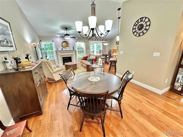 dining area with a fireplace, light wood finished floors, baseboards, ceiling fan, and a chandelier