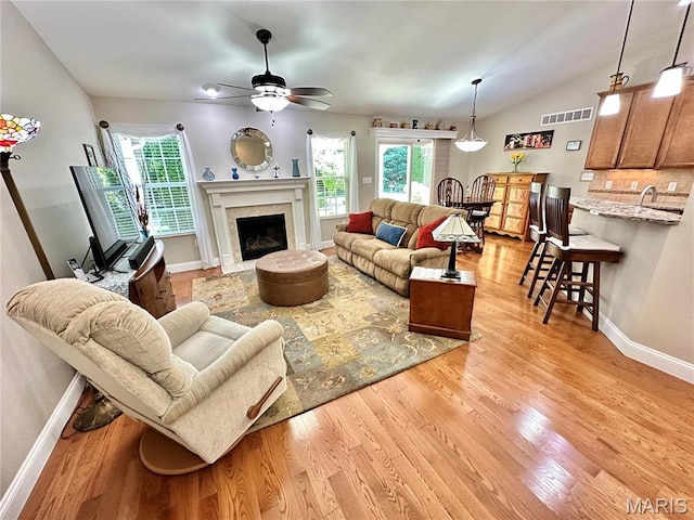 living area featuring ceiling fan, light wood-style floors, baseboards, a high end fireplace, and lofted ceiling