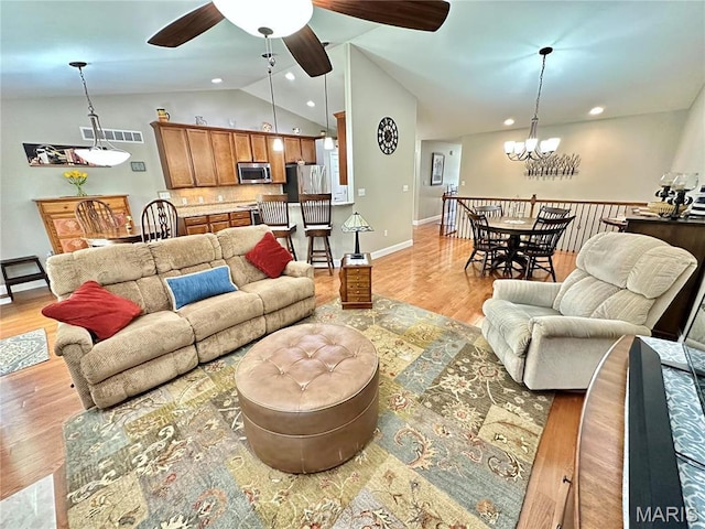 living room with lofted ceiling, light wood finished floors, a chandelier, a ceiling fan, and baseboards