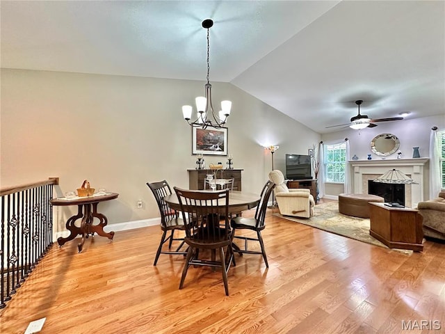 dining space with light wood-style floors, vaulted ceiling, a chandelier, a ceiling fan, and baseboards