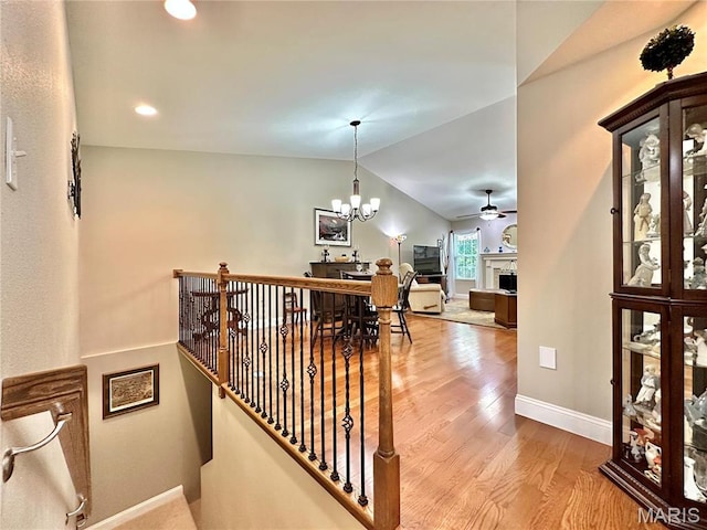 corridor featuring wood finished floors, vaulted ceiling, a chandelier, baseboards, and an upstairs landing