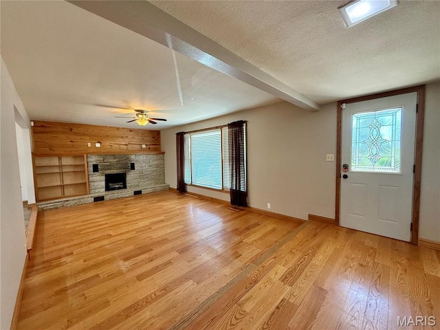 unfurnished living room with light wood finished floors, healthy amount of natural light, a textured ceiling, ceiling fan, and a stone fireplace