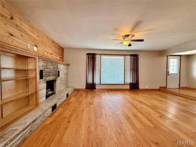 unfurnished living room with a ceiling fan, a fireplace, light wood-type flooring, and baseboards