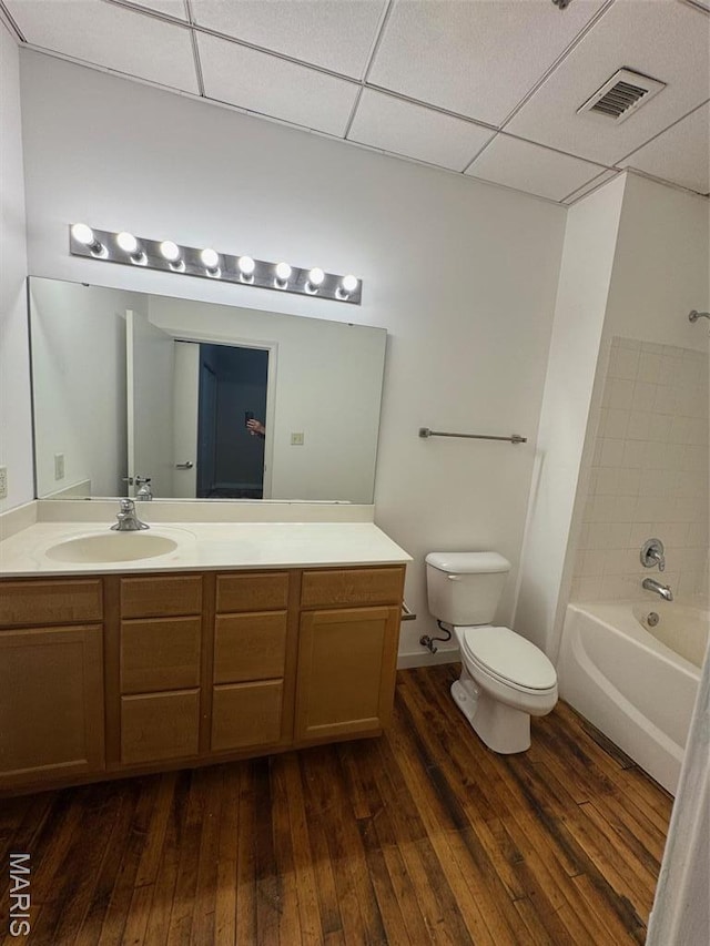 full bathroom featuring toilet, hardwood / wood-style floors, vanity, a drop ceiling, and bathtub / shower combination