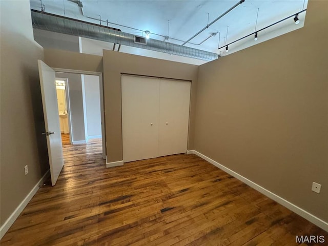unfurnished bedroom with wood finished floors, baseboards, and a closet