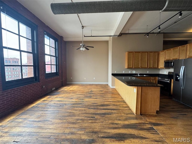 kitchen with black appliances, brick wall, dark countertops, dark wood-style flooring, and a sink