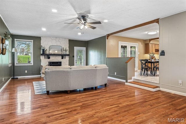 1304 Napoleon Dr, Bonne Terre, MO 63628 - living room featuring wood finished floors, a ceiling fan, baseboards, a textured ceiling, and a stone fireplace