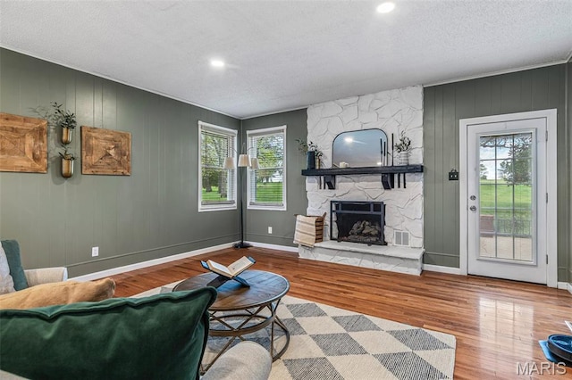 1304 Napoleon Dr, Bonne Terre, MO 63628 - living room featuring healthy amount of natural light, wood finished floors, a stone fireplace, a textured ceiling, and baseboards