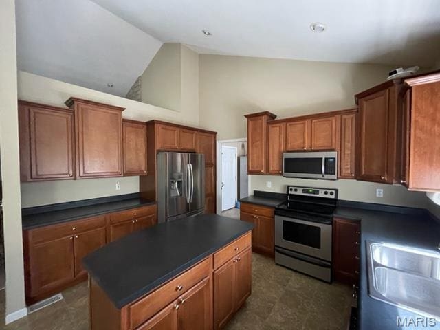 11 Summers Dr, Hawk Point, MO 63349 - kitchen featuring appliances with stainless steel finishes, dark countertops, brown cabinetry, a center island, and high vaulted ceiling