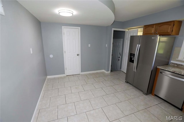 6616 Dunwold Dr, Saint Louis, MO 63134 - kitchen featuring appliances with stainless steel finishes, baseboards, brown cabinetry, light tile patterned floors, and stone counters