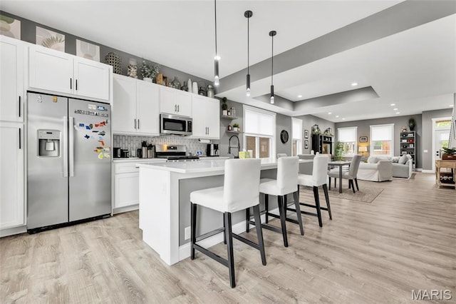 2034 Ann Ave, Saint Louis, MO 63104 - kitchen featuring appliances with stainless steel finishes, light wood-style floors, an island with sink, a breakfast bar, and decorative backsplash