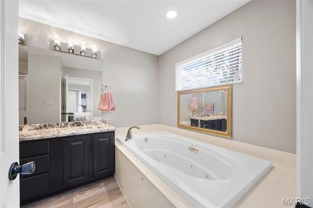full bathroom featuring a whirlpool tub, vanity, and wood finished floors