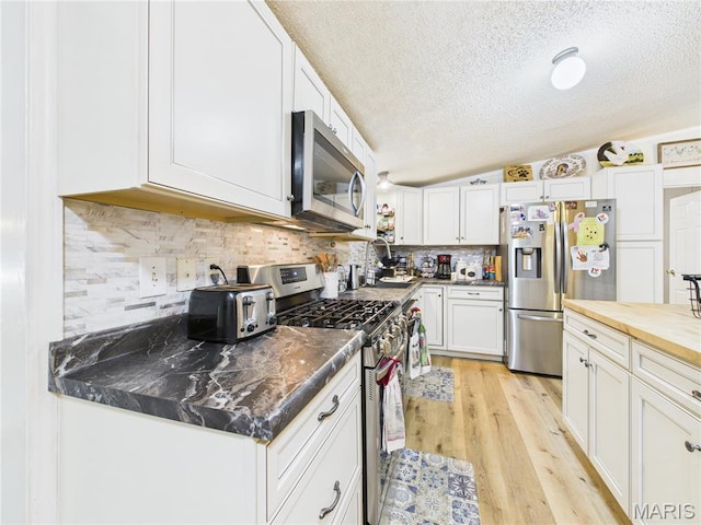 kitchen with stainless steel appliances, a textured ceiling, white cabinets, light wood-style flooring, and backsplash