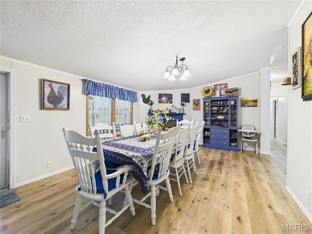 dining room with a chandelier, light wood-style floors, a textured ceiling, ornamental molding, and baseboards