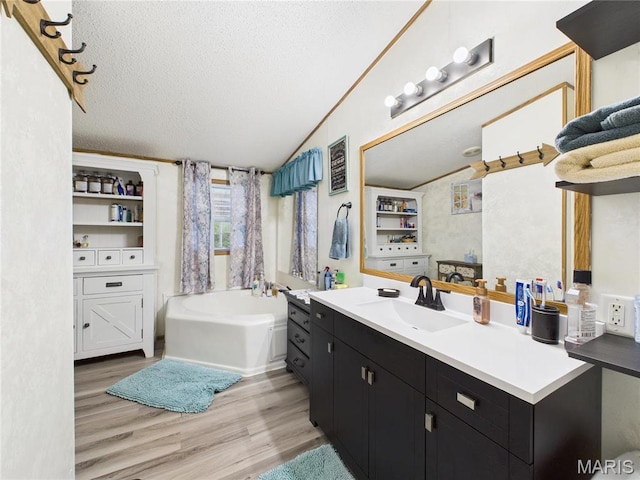 full bathroom with a textured ceiling, wood finished floors, vaulted ceiling, a bath, and vanity