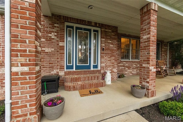 view of exterior entry with covered porch and brick siding