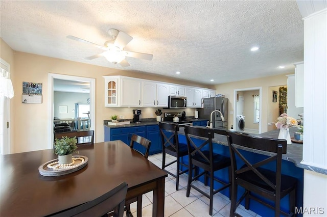 kitchen featuring appliances with stainless steel finishes, dark countertops, light tile patterned flooring, white cabinets, and a kitchen breakfast bar