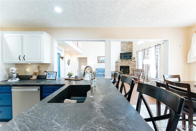 kitchen featuring dishwasher, a sink, a fireplace, white cabinetry, and dark stone countertops