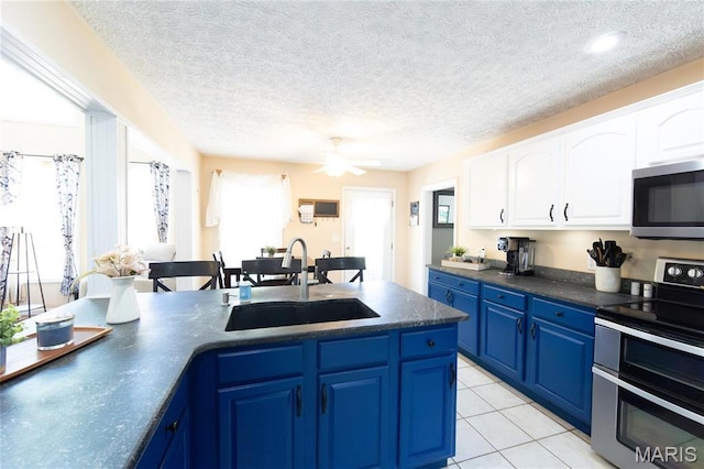 kitchen with appliances with stainless steel finishes, a sink, blue cabinetry, dark countertops, and a textured ceiling