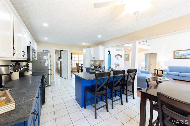 kitchen with dark countertops, stainless steel microwave, white cabinets, a breakfast bar area, and a textured ceiling