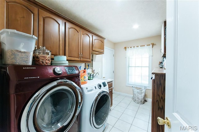 washroom featuring washer and clothes dryer, cabinet space, light tile patterned floors, baseboards, and a textured ceiling