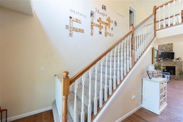 stairway with wood finished floors, a high ceiling, baseboards, and a stone fireplace