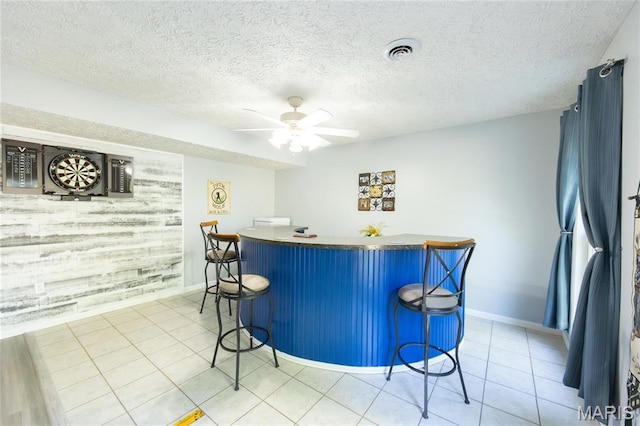 indoor bar featuring baseboards, ceiling fan, light tile patterned flooring, and a textured ceiling
