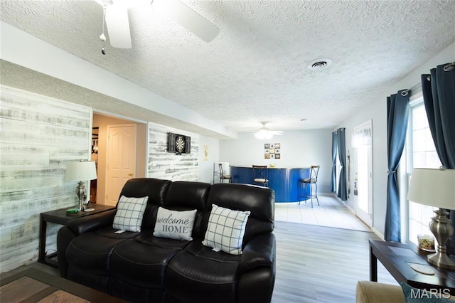 living area featuring a ceiling fan, light wood finished floors, and a textured ceiling