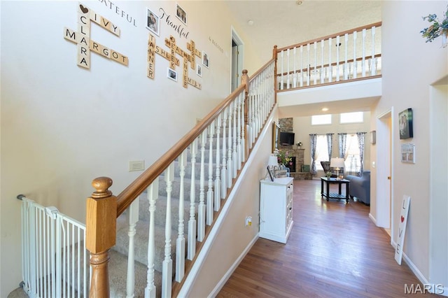 stairway featuring wood finished floors, a high ceiling, and baseboards