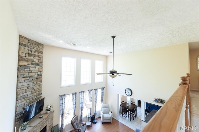 living area with a textured ceiling, a ceiling fan, wood finished floors, a stone fireplace, and baseboards