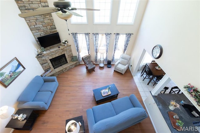 living room featuring a high ceiling, ceiling fan, a fireplace, and wood finished floors