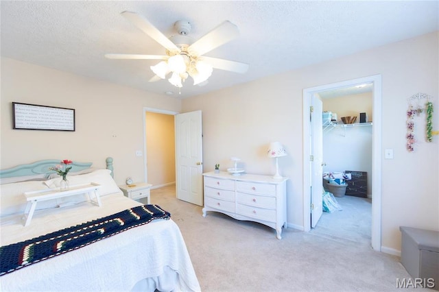 bedroom with a walk in closet, light carpet, ceiling fan, a closet, and a textured ceiling