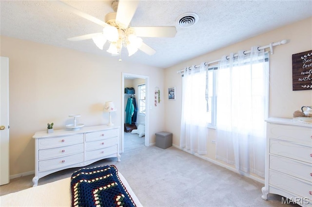 bedroom with light colored carpet, a spacious closet, a textured ceiling, ceiling fan, and baseboards