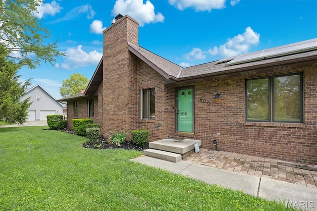 view of front facade featuring a chimney, a front lawn, brick siding, roof mounted solar panels, and a garage