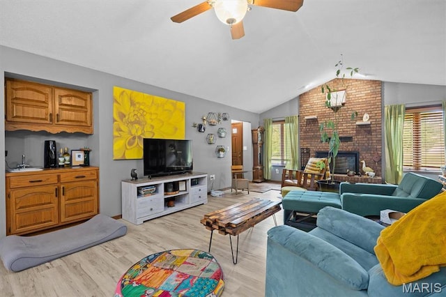 living room with vaulted ceiling, plenty of natural light, light wood-style flooring, a ceiling fan, and a brick fireplace