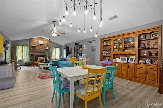 dining area featuring vaulted ceiling, light wood-style floors, a ceiling fan, and a brick fireplace