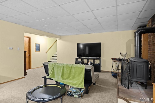carpeted living room with a drop ceiling, a wood stove, stairs, and baseboards