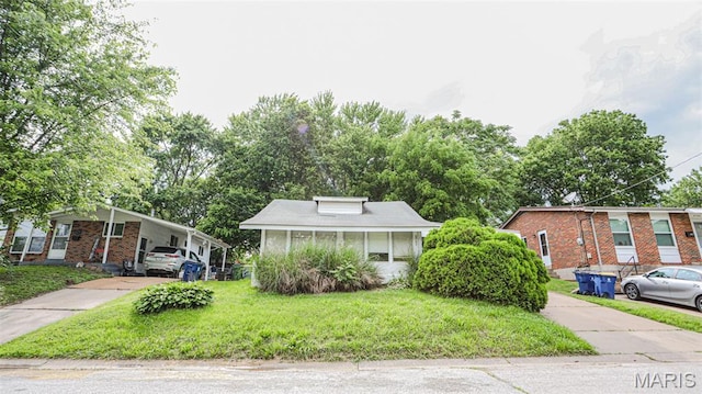 view of front facade featuring concrete driveway, a front lawn, brick siding, and a carport