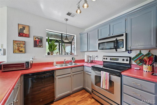 kitchen with stainless steel appliances, a sink, a textured ceiling, light wood-style flooring, and pendant lighting