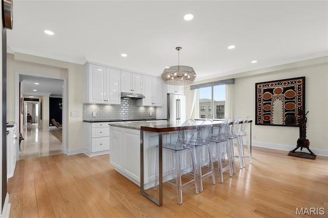 900 S Hanley Rd Unit 15E, Clayton, MO 63105 - kitchen with under cabinet range hood, high end fridge, light wood-style flooring, backsplash, and recessed lighting