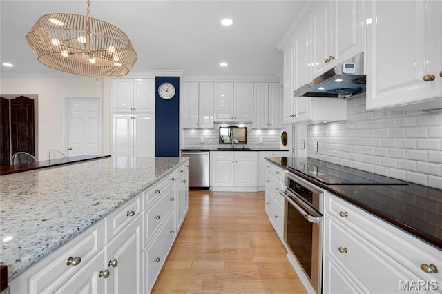 900 S Hanley Rd Unit 15E, Clayton, MO 63105 - kitchen featuring under cabinet range hood, appliances with stainless steel finishes, a chandelier, white cabinetry, and crown molding