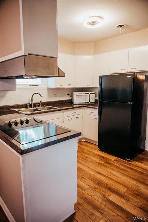 kitchen featuring black appliances, a sink, white cabinets, dark countertops, and light wood-style floors
