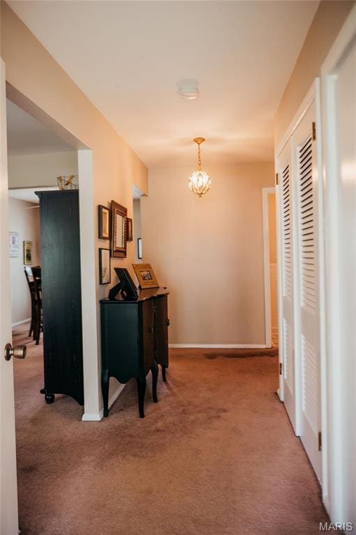hallway with carpet flooring, a chandelier, and baseboards
