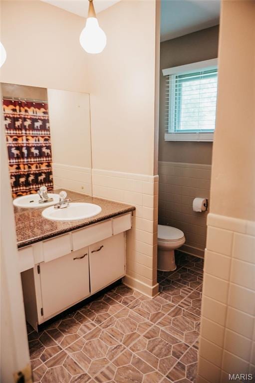 full bathroom with tile walls, wainscoting, toilet, vanity, and curtained shower