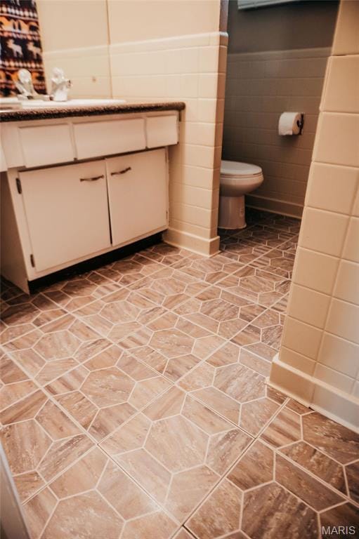 bathroom featuring toilet, tile walls, wainscoting, and vanity