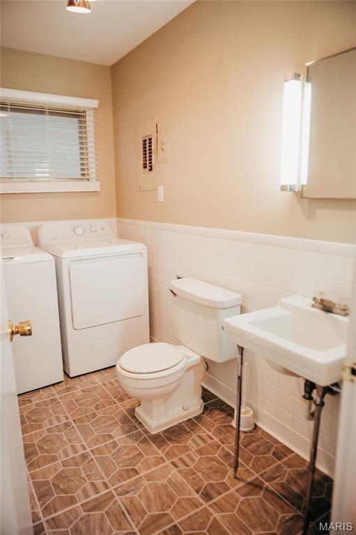 half bath featuring washer and dryer, wainscoting, toilet, and a sink